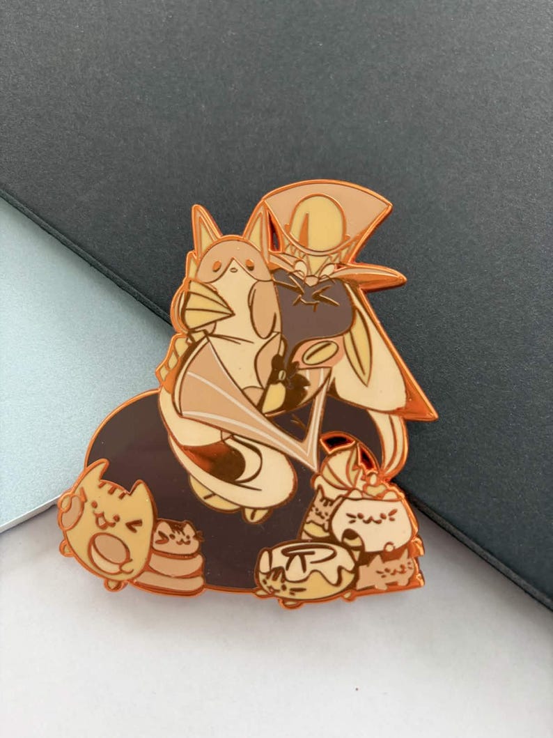 May include: A gold-colored enamel pin featuring a cartoon character with a long hat and cape, surrounded by several small cat-like figures. The pin has a brown and tan color scheme with black accents.