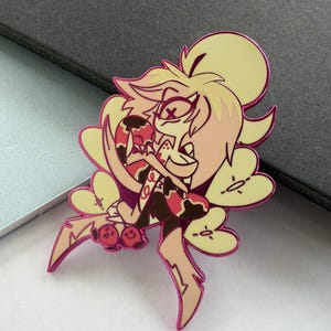 May include: A pin featuring a cartoon character with a yellow and pink color scheme. The character has a stylized design with multiple arms and a smiling expression. The pin has a pink outline and is likely made of metal.