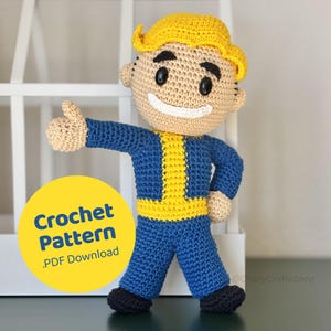 Può includere: Bambola all'uncinetto di un personaggio in tuta blu con dettagli gialli, che fa il pollice in su. La bambola ha un viso sorridente, occhi neri e capelli gialli. Un cerchio giallo con le parole "Crochet Pattern .PDF Download" è nell'immagine.