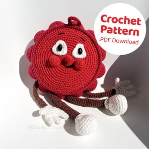 May include: Crochet pattern for a red, round, amigurumi character with brown arms and legs and white hands and feet. The character has a smiling face with black eyes and a black nose. The pattern is available as a PDF download. The text "Crochet Pattern .PDF Download" is in the upper right corner of the image.