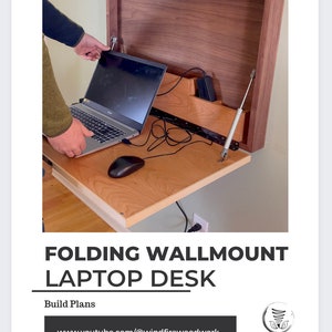 May include: A folding wall-mounted laptop desk made of wood, with a laptop, mouse, and power adapter. The desk is shown in the open position, revealing a light-colored wood surface. The text "FOLDING WALLMOUNT LAPTOP DESK" is displayed.