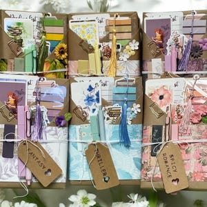 May include: Arrangement of six brown paper packages, each containing stationery and decorative items. Each package is wrapped with twine and includes a tag with a genre label: Fantasy, Thriller, or Spicy Romance. The packages are decorated with flowers and tassels.