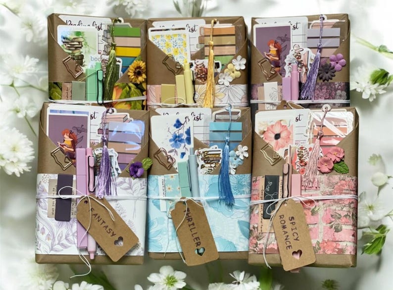 May include: Arrangement of six brown paper packages, each containing stationery and decorative items. Each package is wrapped with twine and includes a tag with a genre label: Fantasy, Thriller, or Spicy Romance. The packages are decorated with flowers and tassels.