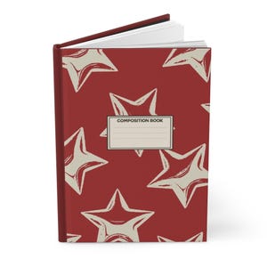 May include: A hardcover composition book with a deep red cover featuring a repeating pattern of off-white stars. A rectangular white label is centered on the front cover with the text "COMPOSITION BOOK" printed in black above three blank lines.
