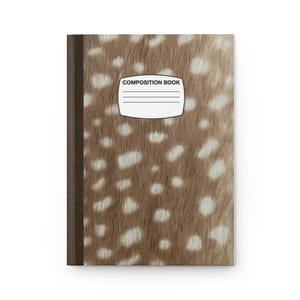 May include: A composition book featuring a brown and white spotted fur pattern on the cover. The notebook has a dark brown spine and a white rectangular label in the center with the text COMPOSITION BOOK and four horizontal lines for writing.