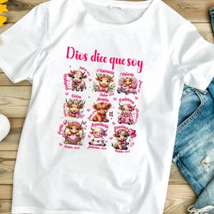 May include: White t-shirt with a pink graphic design featuring a cow with different words and bible verses around it. The text says "Dios dice que soy" which translates to "God says I am".