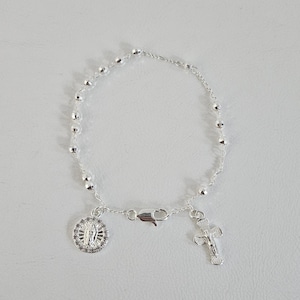 Puede incluir: Una pulsera de rosario plateada con pequeñas cuentas redondas. Incluye un colgante con la imagen de la Virgen María, una cruz y un cierre. Esta pulsera está diseñada para uso religioso y está hecha de plata.