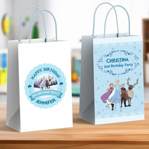 May include: Two white gift bags with pale blue handles. One bag features a blue circular design with the text "Happy Birthday" and "Jennifer". The other bag has a pale blue background with the text "Christina 2nd Birthday Party".