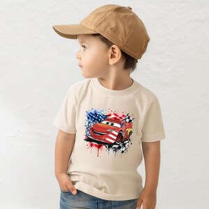 A young boy wearing a baseball cap and a t-shirt with a graphic of a red car and an American flag design.