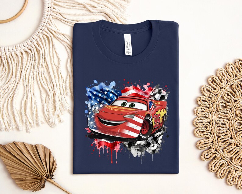 A navy blue t-shirt with a graphic of a red car, featuring an American flag and splatter paint, is displayed on a white background.