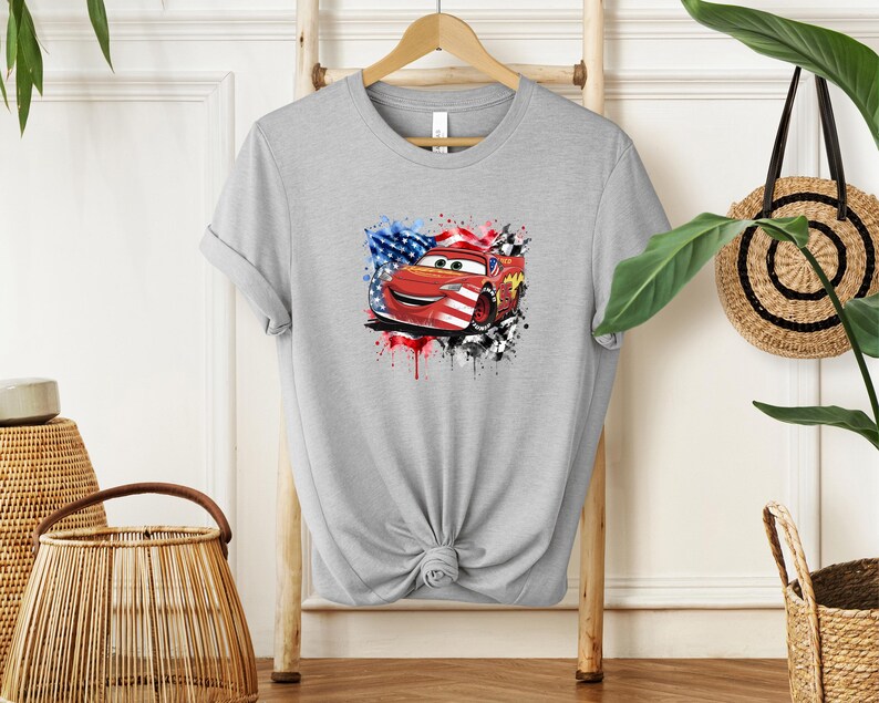 A gray t-shirt with a graphic of a red car and an American flag design, hanging on a wooden hanger.