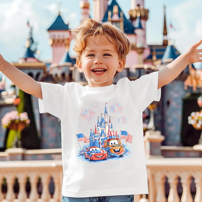 A young boy with blond hair is smiling and raising his arms, wearing a white t-shirt with a graphic of a castle and fireworks.
