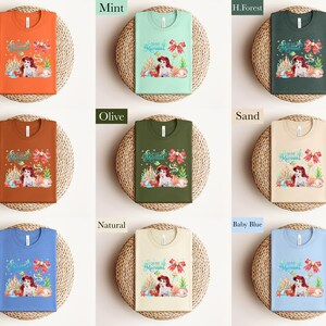 The image is a collage of nine different t-shirt designs, each with a unique color and style. The t-shirts are arranged in a grid pattern, with three rows and three columns. The designs include a mermaid, a forest, and a beach scene, as well as other colorful and whimsical elements.