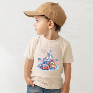 A young boy wearing a baseball cap and a t-shirt with a graphic of a castle and two cars, likely from the Disney Cars movie franchise.