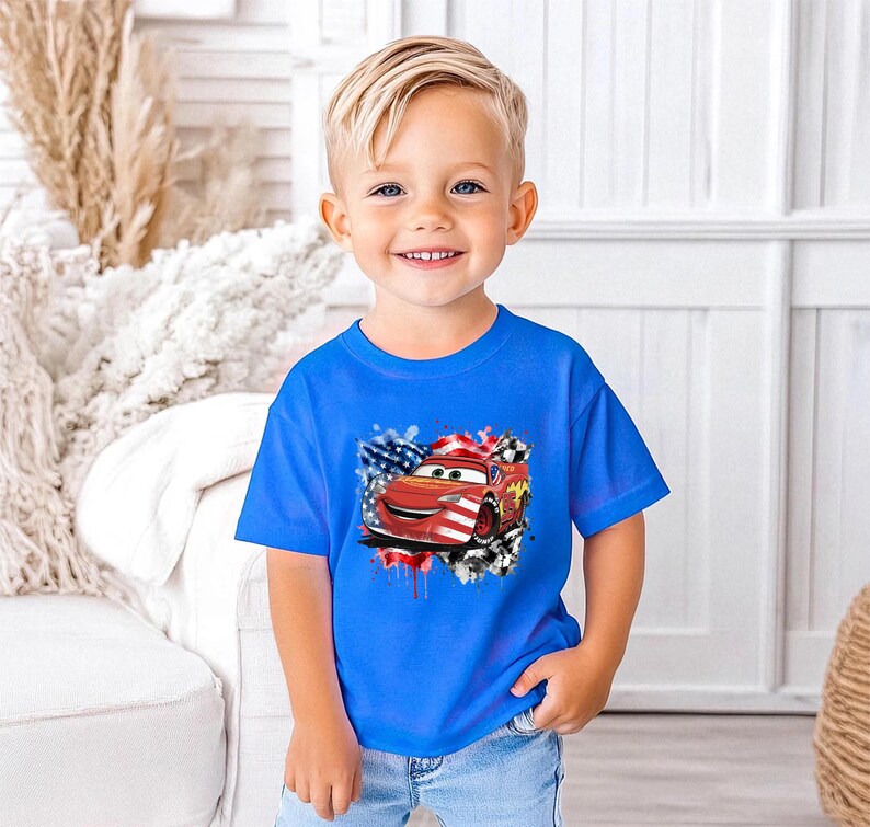 A young boy wearing a blue t-shirt with a graphic of a red car and an American flag design, smiling at the camera.