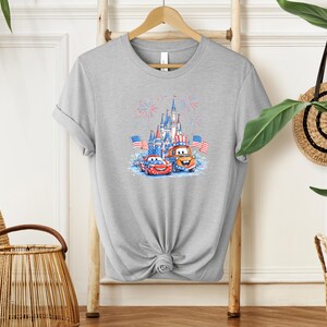 A gray t-shirt with a graphic design featuring a castle, cars, and fireworks, along with American flags.