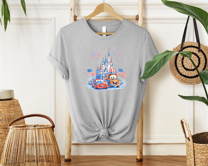 A gray t-shirt with a graphic design featuring a castle, cars, and fireworks, along with American flags.