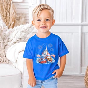 A young boy wearing a blue t-shirt with a Disney Cars graphic and a castle in the background, smiling at the camera.
