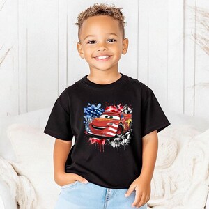 A young boy wearing a black t-shirt with a graphic of a red car and an American flag design.