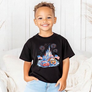 A young boy wearing a black t-shirt with a graphic of a castle and fireworks, smiling at the camera.