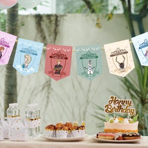 Puede incluir: Una guirnalda con seis banderines con personajes de la pel&iacute;cula Frozen, incluyendo a Anna, Elsa, Kristoff, Olaf y Sven. La guirnalda est&aacute; colgada de una cuerda y forma parte de una decoraci&oacute;n de cumplea&ntilde;os, con una tarta y cupcakes.