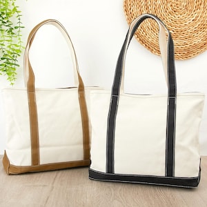 May include: Two canvas tote bags. One is off-white with brown trim and handles. The other is off-white with black trim and handles. Both bags have a rectangular shape and long handles for carrying.
