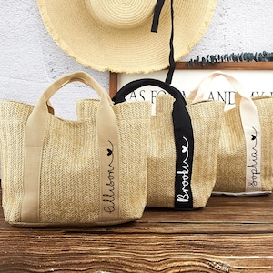 Könnte beinhalten: Drei Strohtaschen mit personalisierten Namen, "Allison", "Brooke" und "Sophia", die auf den Henkeln stehen. Die Taschen sind beige mit schwarzen und weißen Henkeln.