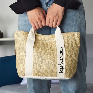 Puede incluir: Una bolsa de mano beige con asas blancas y un coraz&oacute;n negro y el nombre "Sophia" escrito en la parte delantera.