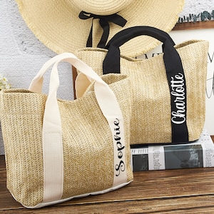 Puede incluir: Dos bolsas de mano de paja con nombres personalizados. La bolsa de la izquierda tiene el nombre "Sophie" bordado en la correa blanca. La bolsa de la derecha tiene el nombre "Charlotte" bordado en la correa negra.