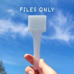 Puede incluir: Una herramienta transparente de forma rectangular con un mango y un pequeño agujero en el extremo se sostiene contra un cielo azul. El texto "FILES ONLY" está en la parte superior de la imagen. La herramienta parece estar hecha de un material translúcido.