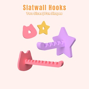 May include: Pink and purple slatwall hooks in cat and star shapes. The hooks have a pegboard design and the text "Slatwall Hooks Two Sizes | Fun Shapes" is at the top.