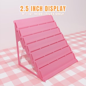 May include: A pink tiered display stand with six horizontal shelves for organizing items. The text at the top reads 2.5 INCH DISPLAY and 9" / 12" WIDE | FILES ONLY. The stand features a triangular side profile and a solid, smooth construction.