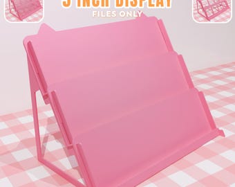 May include: A pink, three-tiered display stand with the text "5 INCH DISPLAY FILES ONLY". The stand is designed to hold files or other small items. The stand is approximately 5 inches wide.