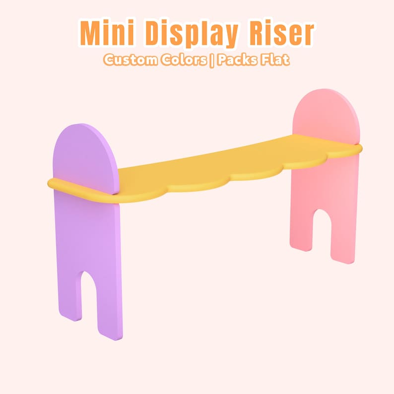 May include: A mini display riser in a pastel color scheme. The display shelf has a yellow scalloped edge, supported by lavender and pink uprights. Text on the image reads "Mini Display Riser" and "Custom Colors | Packs Flat".