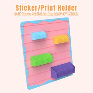 以下が含まれることがあります： 4色の棚が付いたピンクと青のステッカー/プリントホルダー。「Sticker/Print Holder」と「Self Serve Wall Display | 幅6.35cm-12.7cm」の文字が上部に印刷されています。 棚は青、黄、緑、紫です。