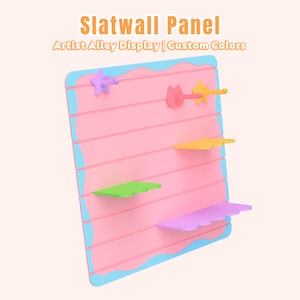 Könnte beinhalten: Eine rosa Lamellenwand mit einem hellblauen wellenförmigen Rand und dem Text Slatwall Panel Artist Alley Display | Custom Colors. Das Paneel enthält verschiedene bunte Regale und Haken in Stern- und Katzenform, darunter in Gelb, Grün und Violett.