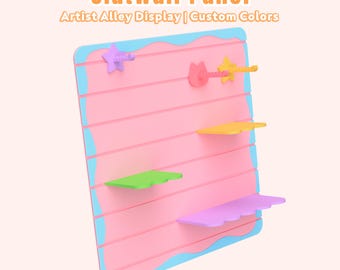 May include: A pink slatwall panel with a light blue wavy border, featuring the text Slatwall Panel Artist Alley Display | Custom Colors. The panel includes various colorful shelves and hooks in star and cat shapes, including yellow, green, and purple.
