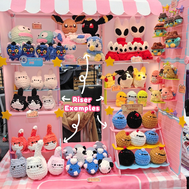 May include: A display of handmade crochet plush toys, including various characters and animals. The display features a pink and white booth with multiple shelves, showcasing the colorful creations. The toys include cats, penguins, and other creatures.