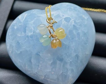 May include: A gold chain necklace featuring a cluster of four small, carved gemstone flower charms in translucent shades of white, pale green, yellow, and orange, suspended from a circular gold clasp.