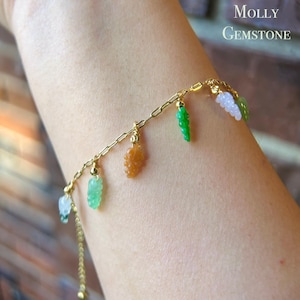May include: A gold chain bracelet featuring gemstone charms in the shape of leaves and grapes. The charms are in shades of green, orange, and white. The text "Molly Gemstone" is visible in the upper right corner.