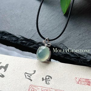 May include: A silver pendant necklace featuring a pale green oval gemstone. The pendant hangs from a black cord. The text "MollyGemstone" is visible on the right side of the image.