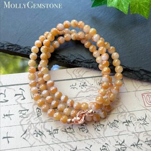 Op de afbeelding: Een armband met meerdere strengen, bestaande uit gepolijste, ronde, doorschijnende oranje en witte kralen. De armband is voorzien van een metalen sluiting in roségoudkleur. De tekst MOLLYGEMSTONE is zichtbaar in de linkerbovenhoek.