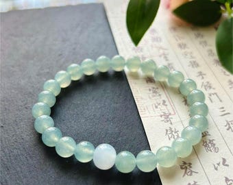 May include: A light blue beaded bracelet with a single white bead. The bracelet is made of round, polished beads and is displayed on a dark gray surface. The bracelet is labeled "MollyGemstone".