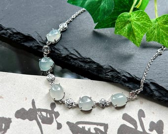 May include: A silver-toned chain bracelet featuring five smooth, oval-shaped pale green cabochon gemstones. The bracelet includes small, circular metal spacers with intricate detailing between each gemstone. The text MOLLYGEMSTONE is visible.
