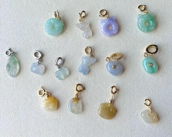 May include: A collection of fourteen small gemstone charms in various shapes and colors, including light green, lavender, yellow, and white, each attached to a gold or silver-toned metal jump ring. The charms feature smooth, polished surfaces.