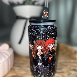 Peut inclure: Un gobelet noir &agrave; paillettes avec des personnages de dessins anim&eacute;s d'une s&eacute;rie fantastique populaire. Le gobelet a un couvercle noir, une paille transparente et une petite figurine sur le dessus. Les personnages sont en uniforme scolaire.