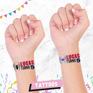 May include: Two temporary tattoos with a black spider and the text "Lucas Turns 5" in red and blue. The tattoos are on a person's wrist.