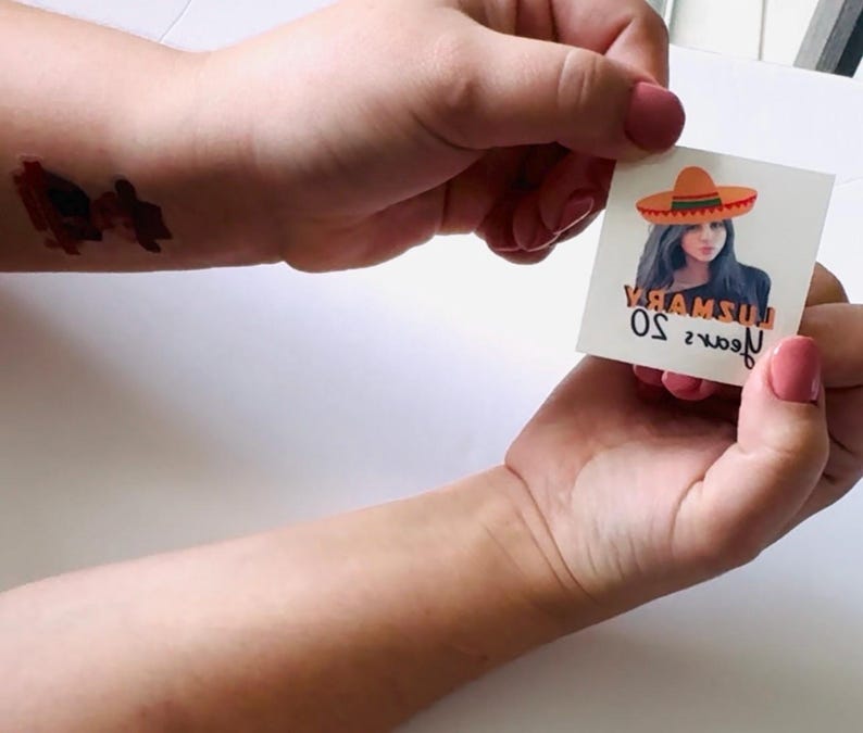 May include: A temporary tattoo depicting a woman in a sombrero. The image includes the text "YAMSU 50 years". The tattoo is held between two hands with pink nail varnish. A puzzle piece tattoo is visible on the wrist.