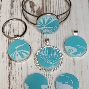 May include: A set of six turquoise blue and white patterned glass cabochons with silver settings. The cabochons are in various shapes and sizes, including round, oval, and square. The cabochons are perfect for jewelry making, such as necklaces, earrings, bracelets, and rings.