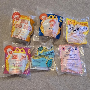 May include: Six sealed McDonald's Happy Meal plastic bags containing various promotional toys. The bags feature colorful graphics, including Ronald McDonald, Disney characters, and text such as Mickey & Friends Adventure at Walt Disney World.